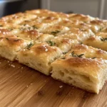Freshly baked sourdough discard focaccia with golden crust, rosemary topping, and airy texture on a wooden table.